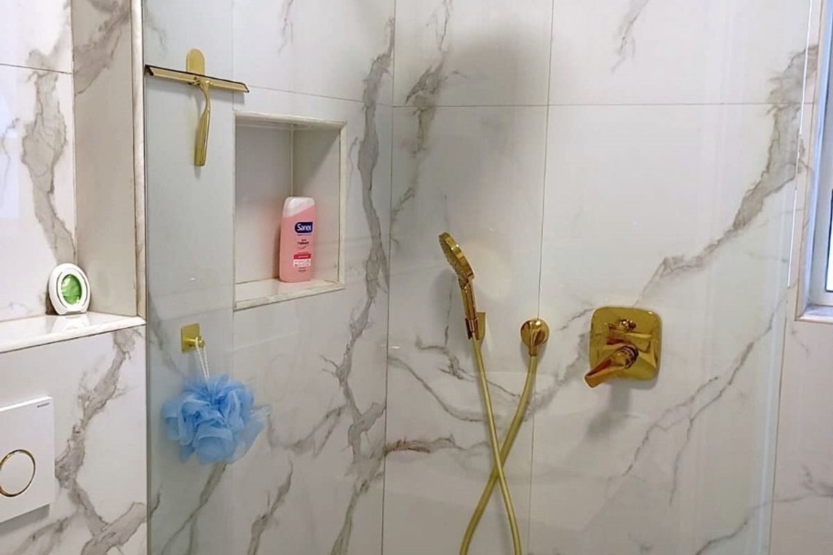 Modern bathroom shower enclosure featuring marble-look wall tiles, mosaic floor tiling, and premium gold-finish shower fixtures with a built-in storage niche.
