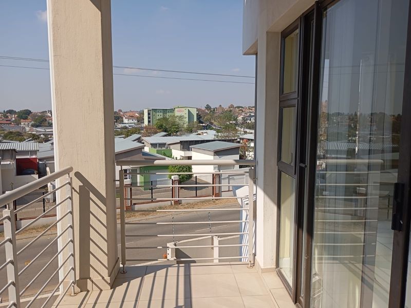 A clean, modern balcony featuring tiled flooring, a metal balustrade, and a sliding glass door, offering an elevated view of the surrounding neighborhood.