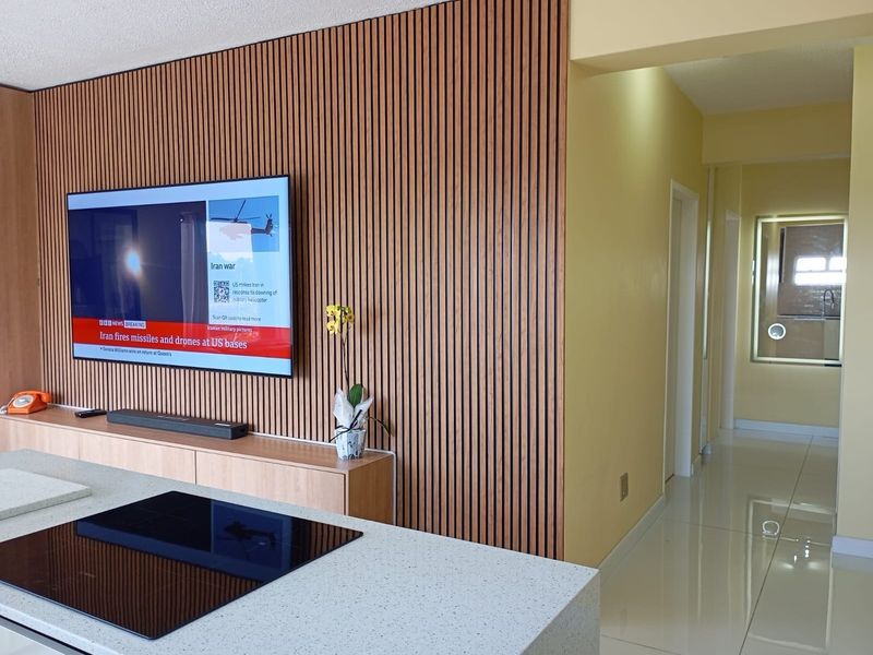 Modern open-plan living area featuring a stylish slatted timber feature wall, built-in media console, and a sleek kitchen island with an integrated induction cooktop.