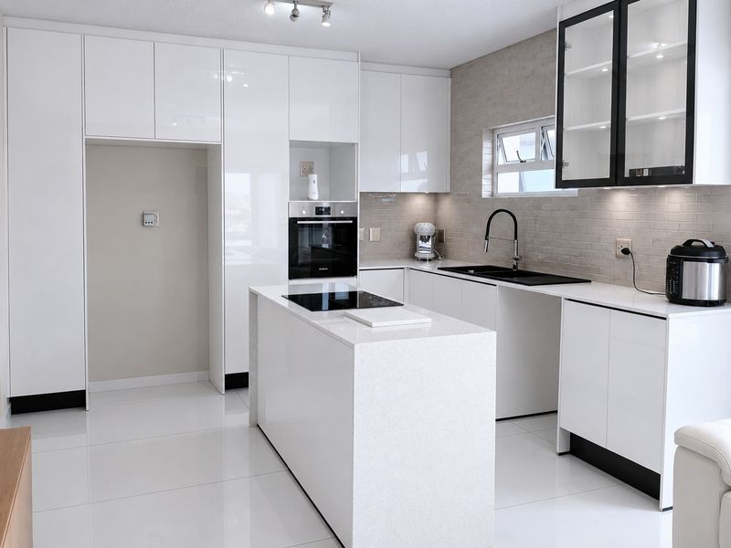 Modern kitchen featuring high-gloss white cabinetry, a central island with an induction hob, quartz countertops, and a stylish subway tile backsplash.