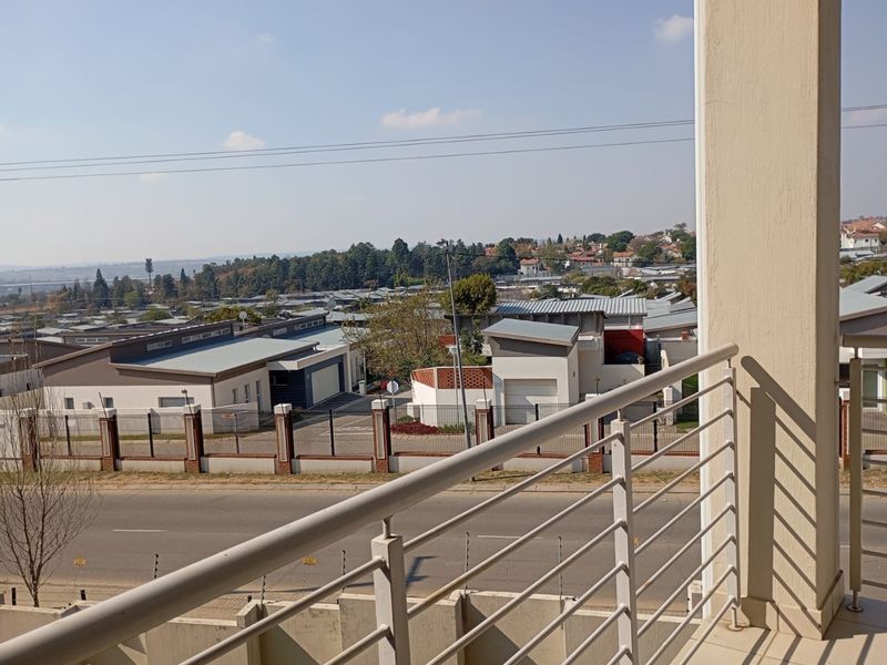 An elevated view from a balcony overlooking the surrounding neighbourhood, street, and nearby commercial buildings.