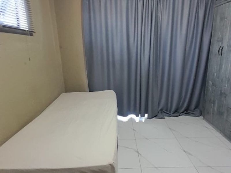 A bedroom featuring white tiled flooring, a curtain rail, and venetian blinds, providing a functional and neutral living space.
