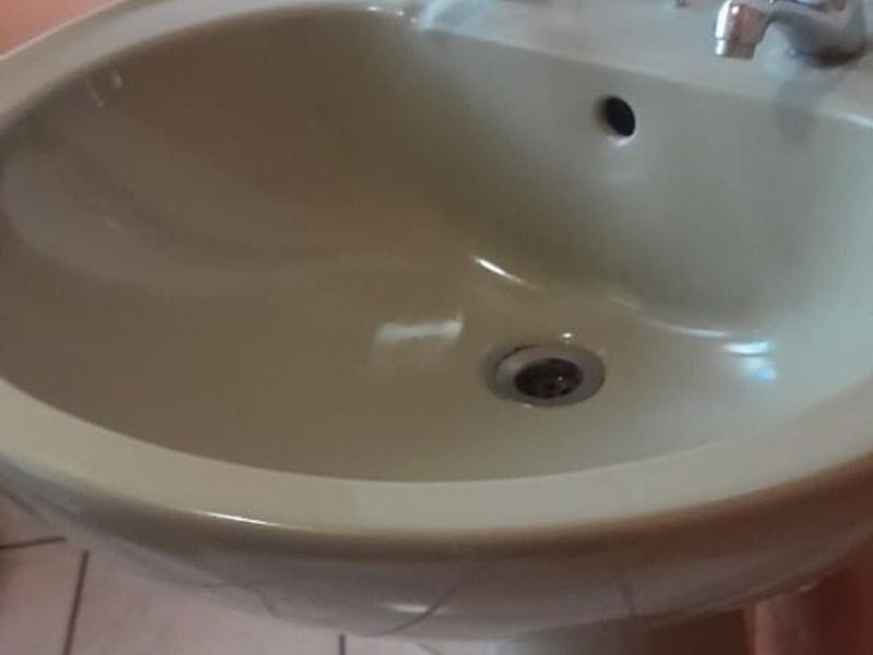 A close-up view of a dated pedestal basin in a bathroom featuring ceramic wall and floor tiles.