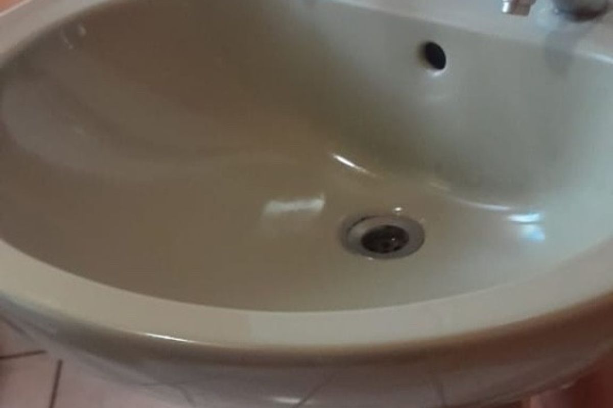 A close-up view of a dated pedestal basin in a bathroom featuring ceramic wall and floor tiles.