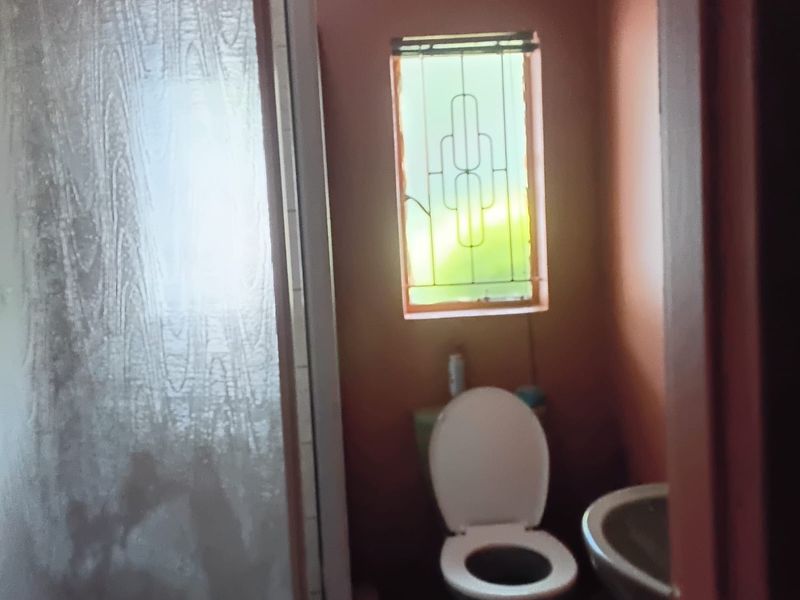 A compact bathroom featuring a shower enclosure, toilet, and washbasin, with a window fitted with security bars.