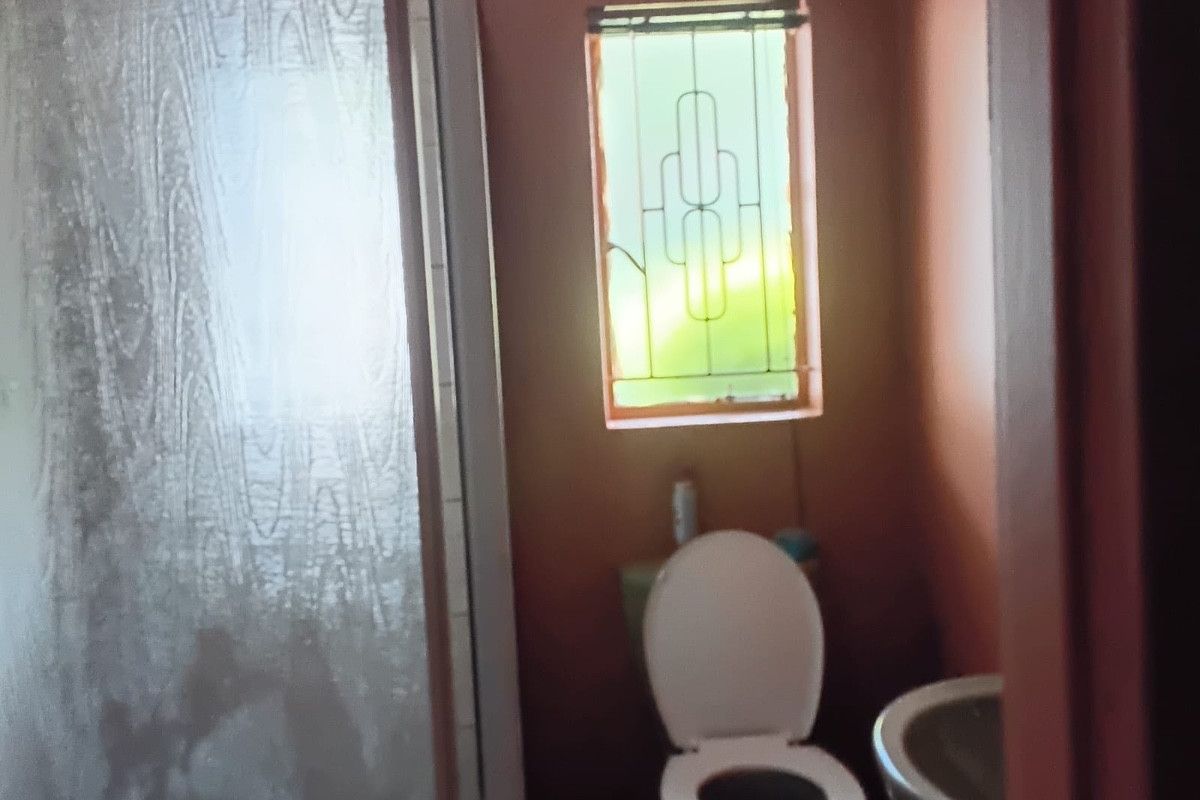 A compact bathroom featuring a shower enclosure, toilet, and washbasin, with a window fitted with security bars.