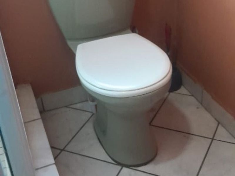 A functional bathroom space featuring a standard toilet, tiled flooring, and a window for natural light.