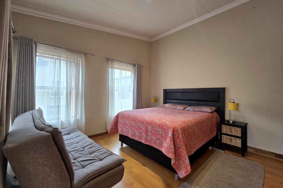 A well-lit bedroom featuring laminate flooring, neutral wall tones, and dual windows with installed curtain rods.