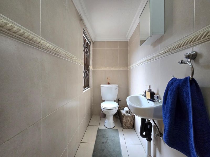 A compact bathroom featuring neutral ceramic wall and floor tiles, a pedestal basin, and a standard toilet with security bars on the window.