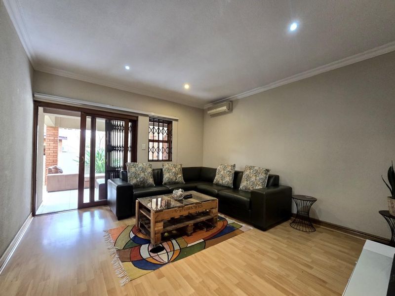 A well-maintained living room featuring laminate flooring, recessed lighting, and a sliding glass door providing access to an outdoor patio area.
