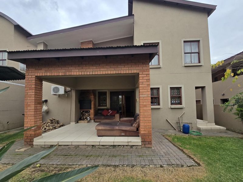 Rear view of the property featuring a covered brick patio with a built-in braai, tiled flooring, and access to a small garden area.