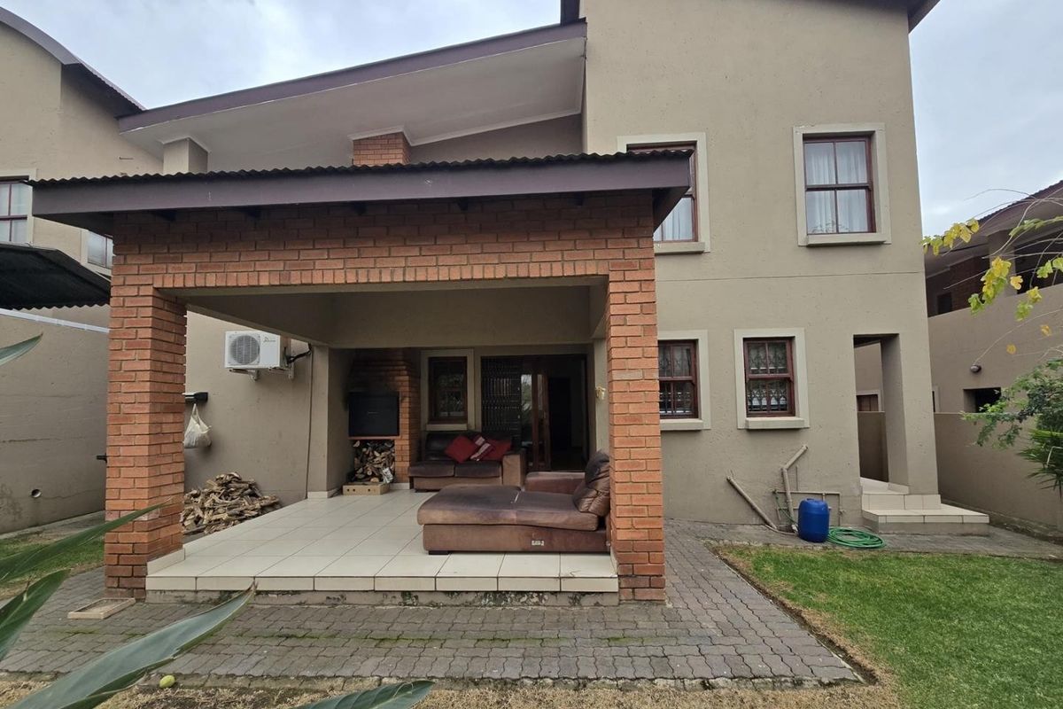 Rear view of the property featuring a covered brick patio with a built-in braai, tiled flooring, and access to a small garden area.