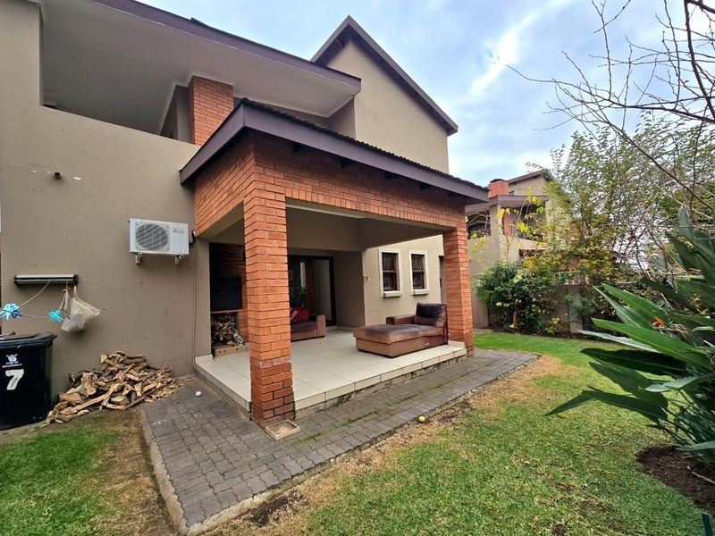A covered patio area featuring brick pillars, tiled flooring, and a built-in braai, overlooking a private garden space.