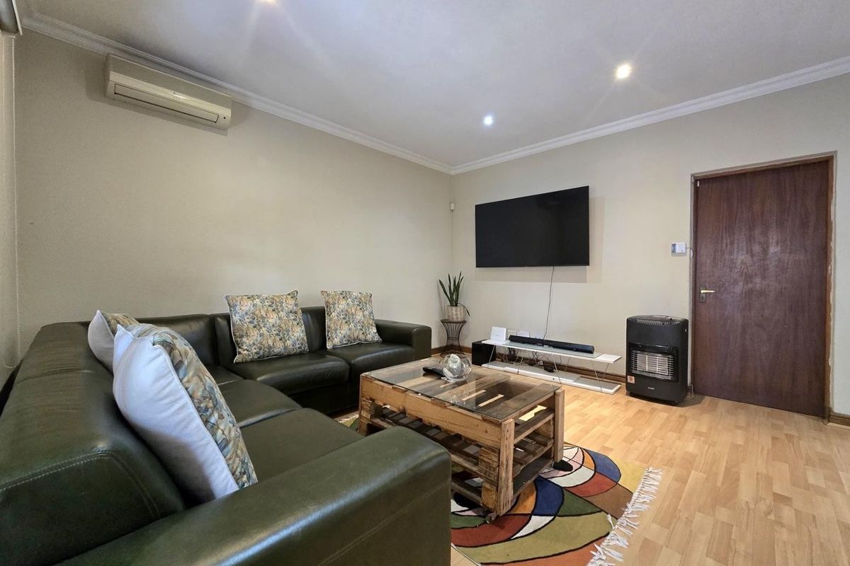 A comfortable living room featuring laminate flooring, recessed downlighting, and a wall-mounted air conditioning unit, providing a functional and well-lit space.