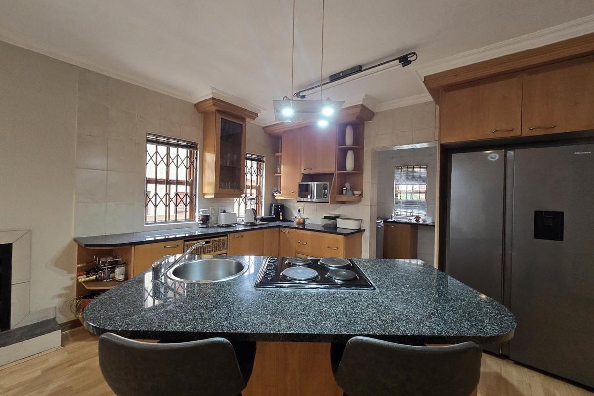A functional kitchen featuring a central island with an integrated hob and sink, granite countertops, and ample wooden cabinetry with a scullery area.