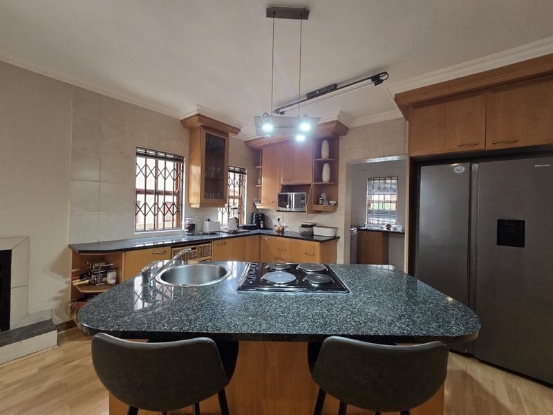 A functional kitchen featuring a central island with an integrated hob and sink, granite countertops, and ample wooden cabinetry with a scullery area.