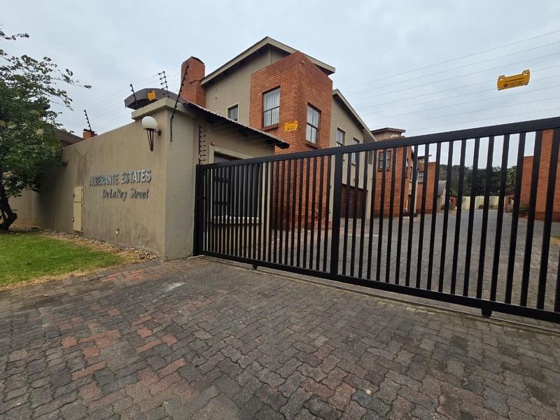 Front entrance view of Alberante Estates featuring a secure electric sliding gate, perimeter wall with electric fencing, and paved driveway access.