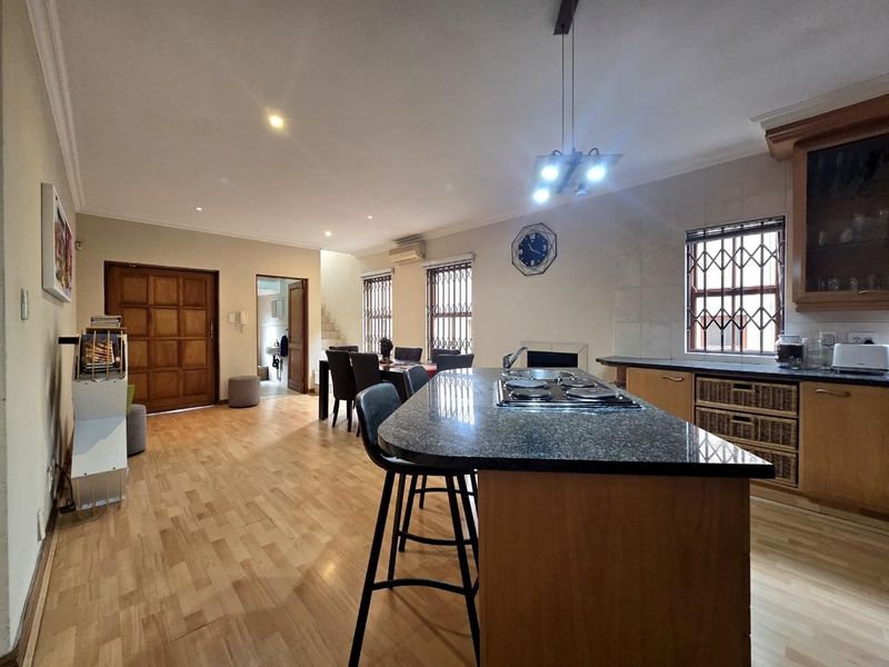 Open-plan living and kitchen area featuring a central island with a built-in hob, wooden flooring, and ample natural light through security-barred windows.