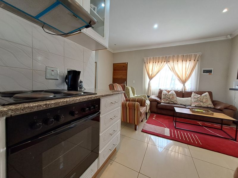 Open-plan living area featuring a functional kitchen with built-in oven and hob, flowing into a comfortable lounge space with tiled flooring throughout.