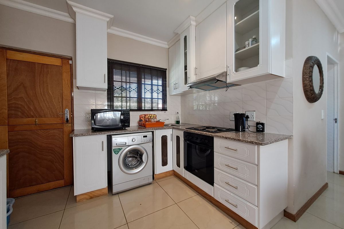 A well-maintained kitchen featuring white cabinetry, granite countertops, built-in oven and hob, tiled backsplash, and integrated laundry appliance space.