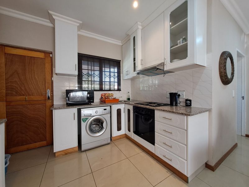 A well-maintained kitchen featuring white cabinetry, granite countertops, built-in oven and hob, tiled backsplash, and integrated laundry appliance space.