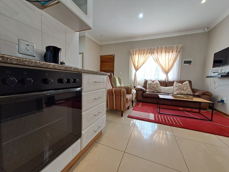 Open-plan living area featuring a modern kitchen with built-in oven, granite countertops, and tiled flooring, seamlessly flowing into the lounge space.