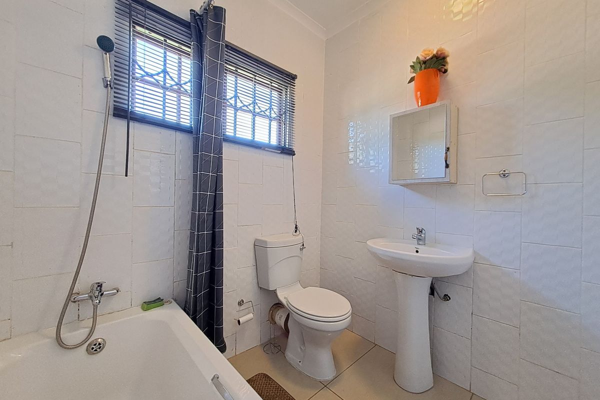 A functional bathroom featuring a pedestal sink, toilet, and bathtub with tiled walls and floor, offering a clean but dated aesthetic.