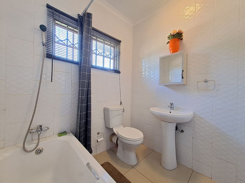 A functional bathroom featuring a pedestal sink, toilet, and bathtub with tiled walls and floor, offering a clean but dated aesthetic.