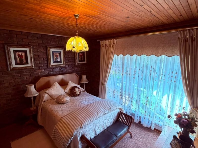 A cozy bedroom featuring a warm timber tongue and groove ceiling and a textured exposed brick feature wall with large window access.
