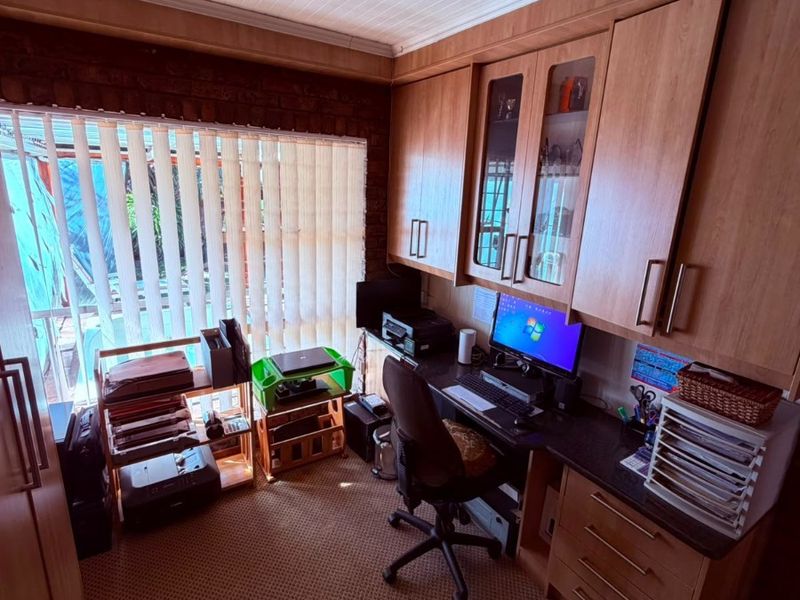 A functional home office featuring extensive built-in cabinetry, a desk workspace, vertical blinds, and track lighting.