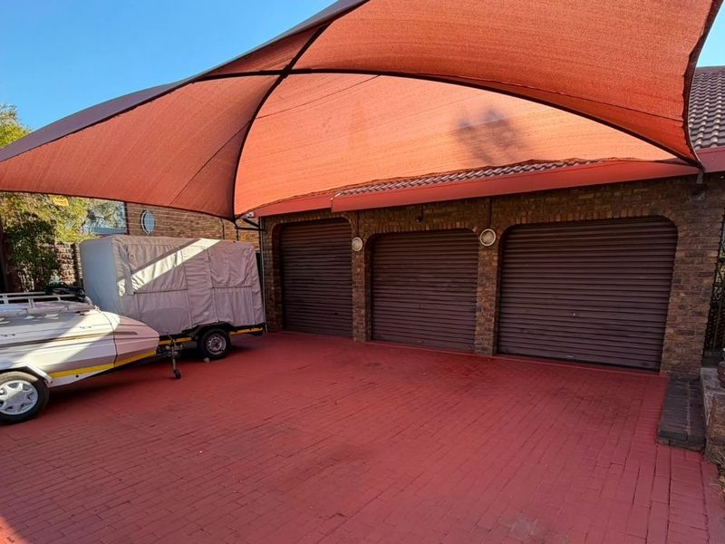 A triple garage with a large shade sail covering the paved driveway area, providing ample parking space.