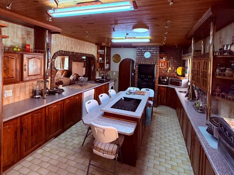 Spacious kitchen featuring extensive timber cabinetry, a central island with integrated cooktop, brick accents, and a warm timber-paneled ceiling.