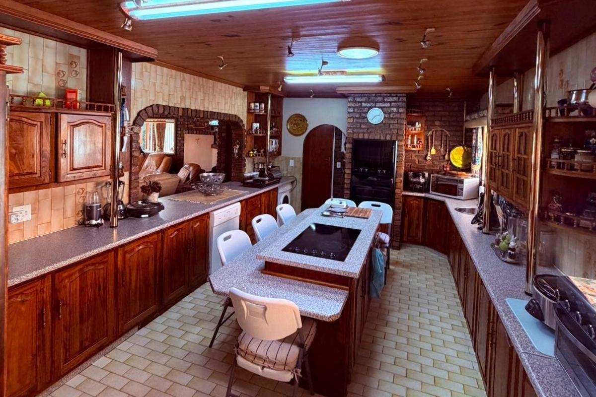 Spacious kitchen featuring extensive timber cabinetry, a central island with integrated cooktop, brick accents, and a warm timber-paneled ceiling.
