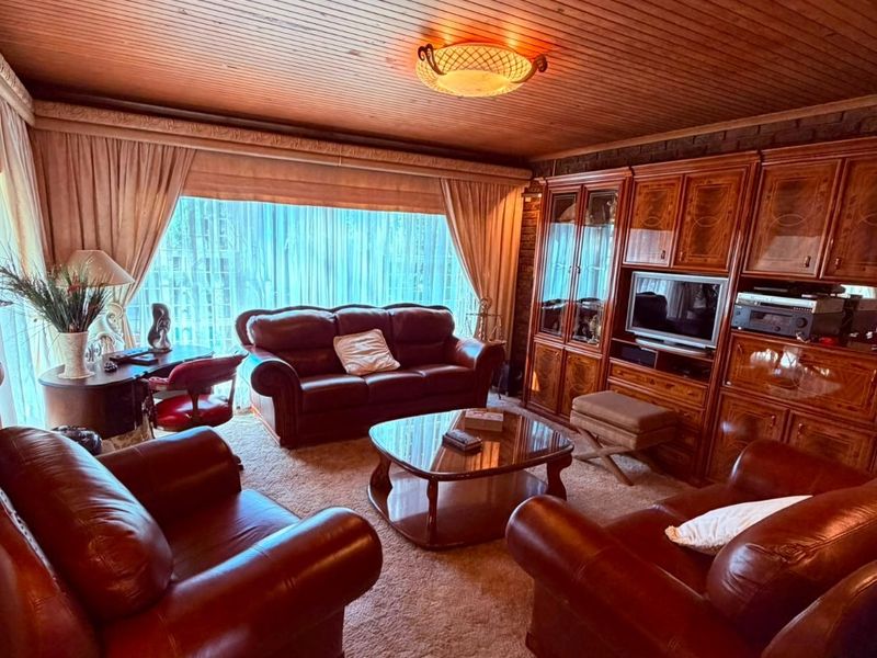 A traditional living room featuring a timber-clad ceiling, wall-to-wall built-in cabinetry, and carpeted flooring, offering a classic and cozy atmosphere.