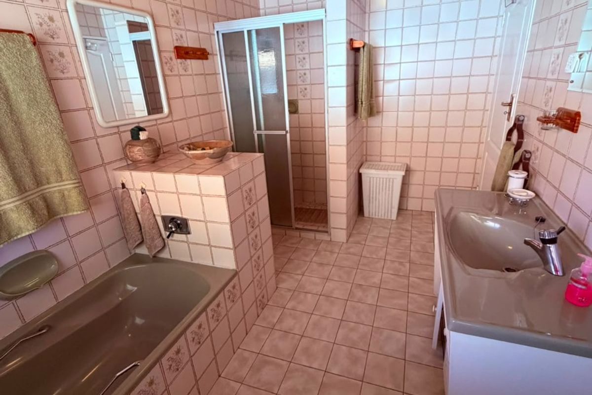 A functional bathroom featuring a built-in bathtub, separate shower enclosure, and vanity basin with tiled finishes and a timber ceiling.