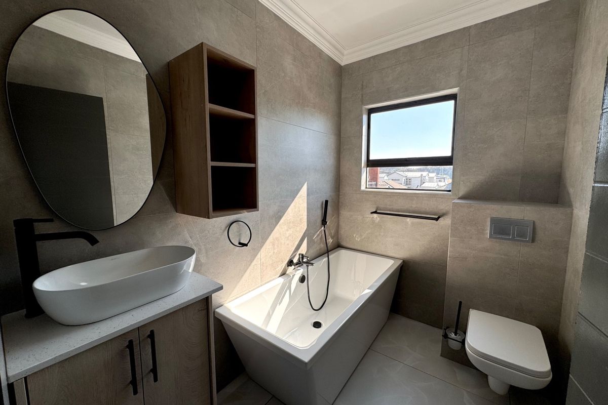 Modern bathroom featuring a sleek freestanding bathtub, wall-mounted toilet with concealed cistern, vessel sink vanity, and contemporary large-format wall tiles.