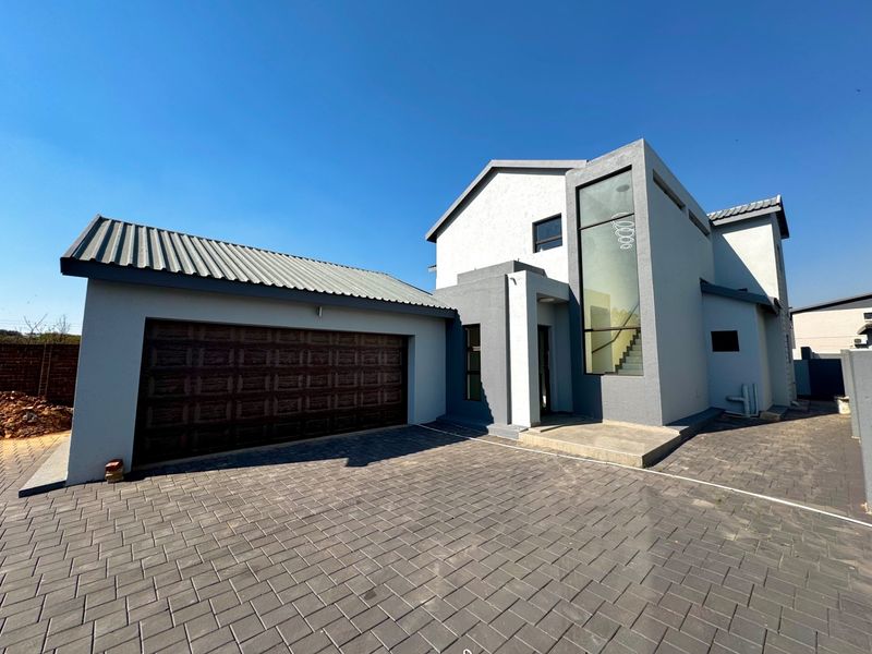 Modern double-storey residential home featuring a paved driveway, integrated double garage, and a striking full-height glass window at the entrance.