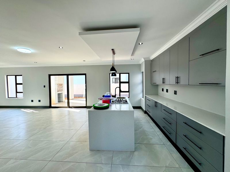 Modern open-plan kitchen featuring sleek grey cabinetry, stone countertops, a central island with a gas hob, and large sliding doors leading to the patio.