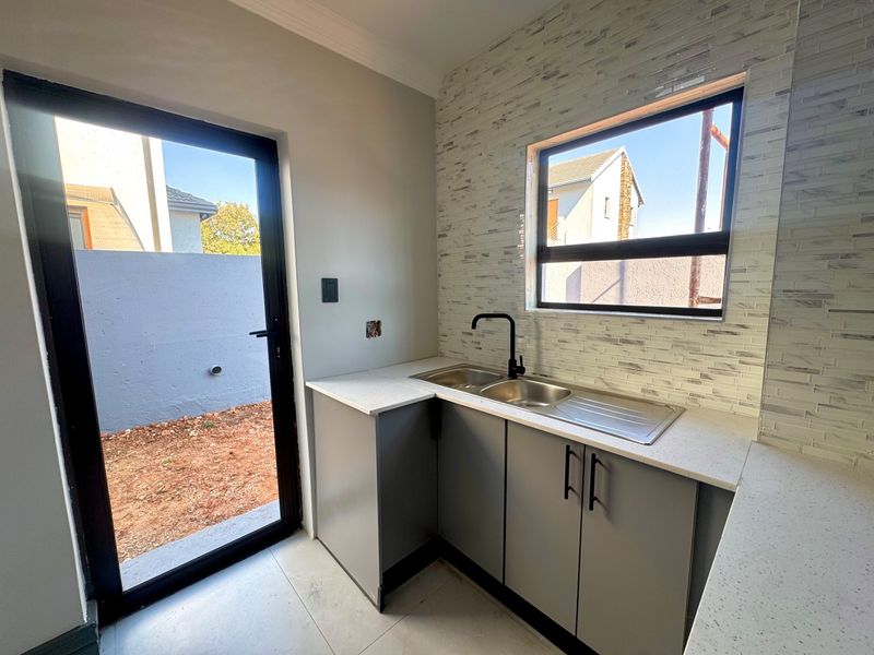 A modern, compact scullery featuring grey cabinetry, stone-look countertops, a stainless steel sink with a black mixer tap, and a tiled backsplash.