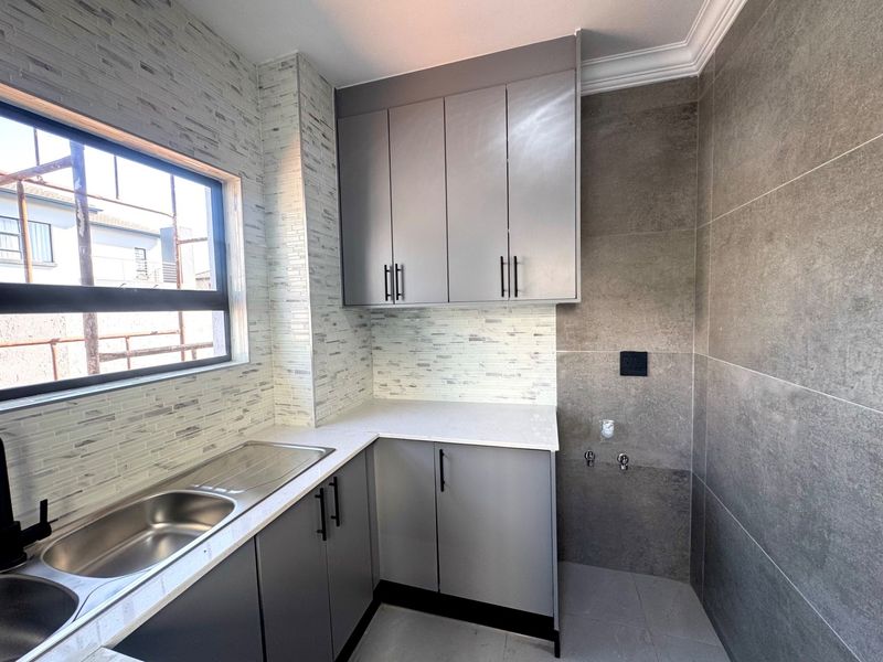 A modern, well-appointed laundry room featuring sleek grey cabinetry, stone countertops, a stainless steel sink, and contemporary large-format wall tiling.