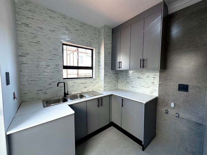 A modern, newly renovated kitchen featuring grey cabinetry, stone countertops, a double sink with black fixtures, and a stylish mosaic tile backsplash.