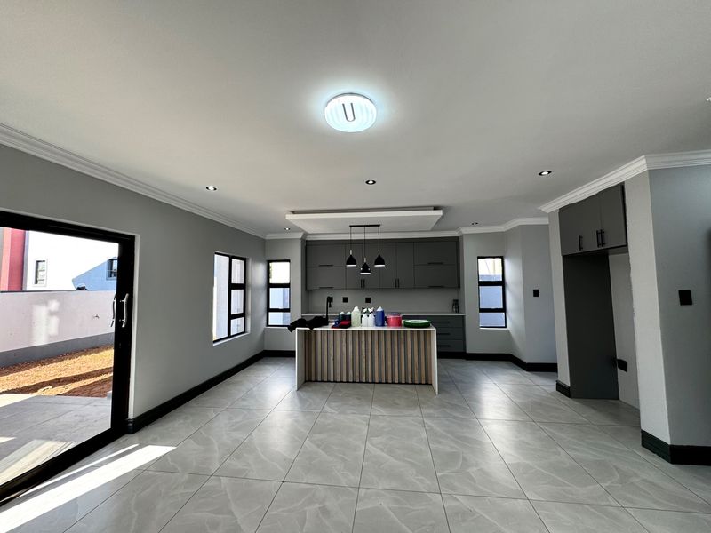 Modern open-plan kitchen featuring a central island, sleek grey cabinetry, tiled flooring, and direct access to the outdoor patio area.
