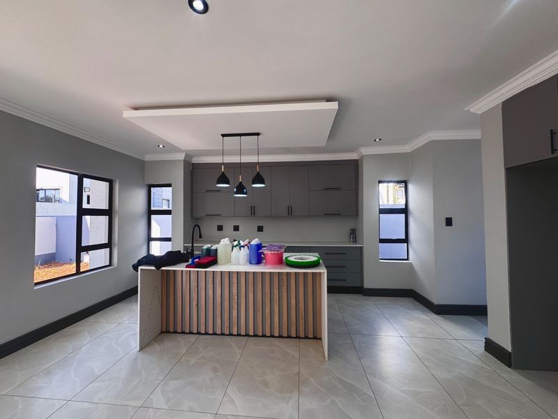 Modern kitchen featuring a central island with timber slat detailing, sleek grey cabinetry, stone countertops, and large windows providing ample natural light.