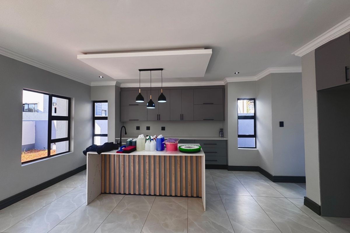 Modern kitchen featuring a central island with timber slat detailing, sleek grey cabinetry, stone countertops, and large windows providing ample natural light.
