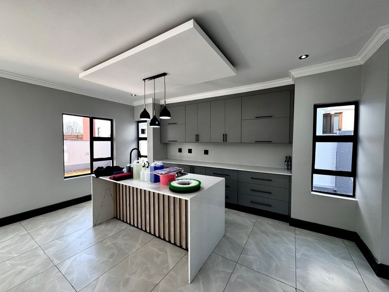 Modern kitchen featuring a central island with quartz countertops, sleek grey cabinetry, pendant lighting, and large format tiled flooring.