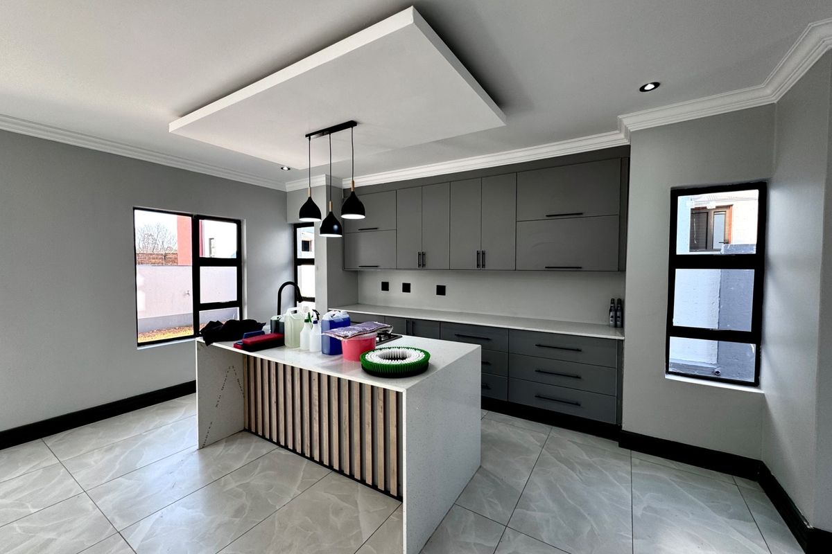 Modern kitchen featuring a central island with quartz countertops, sleek grey cabinetry, pendant lighting, and large format tiled flooring.