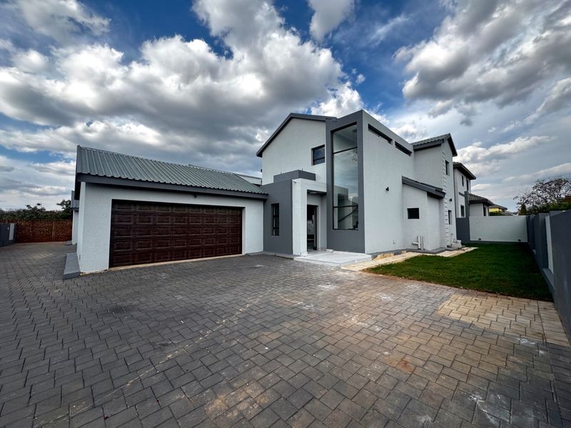 Modern double-story residential property featuring a paved driveway, double garage, and striking full-height glass window detail on the front facade.
