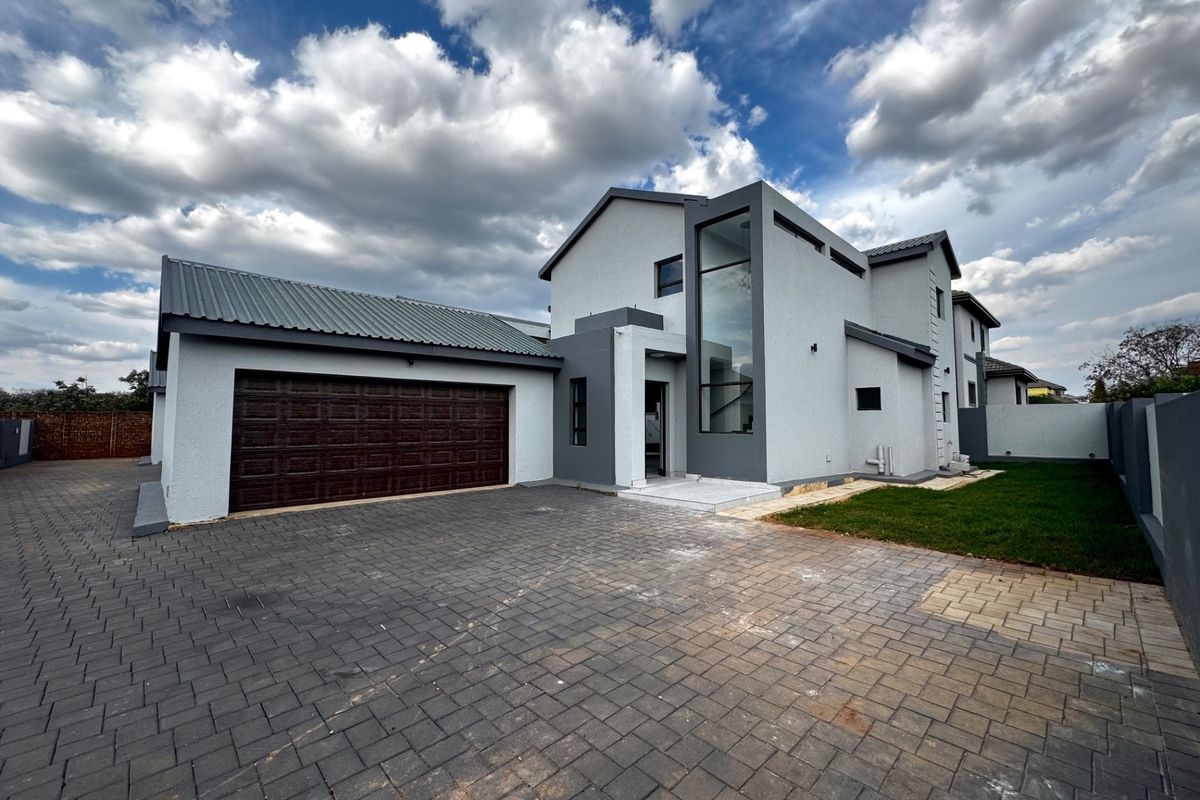 Modern double-story residential property featuring a paved driveway, double garage, and striking full-height glass window detail on the front facade.
