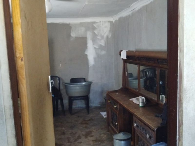 A bedroom space requiring significant renovation, featuring unfinished plaster walls, worn flooring, and dated ceiling finishes.