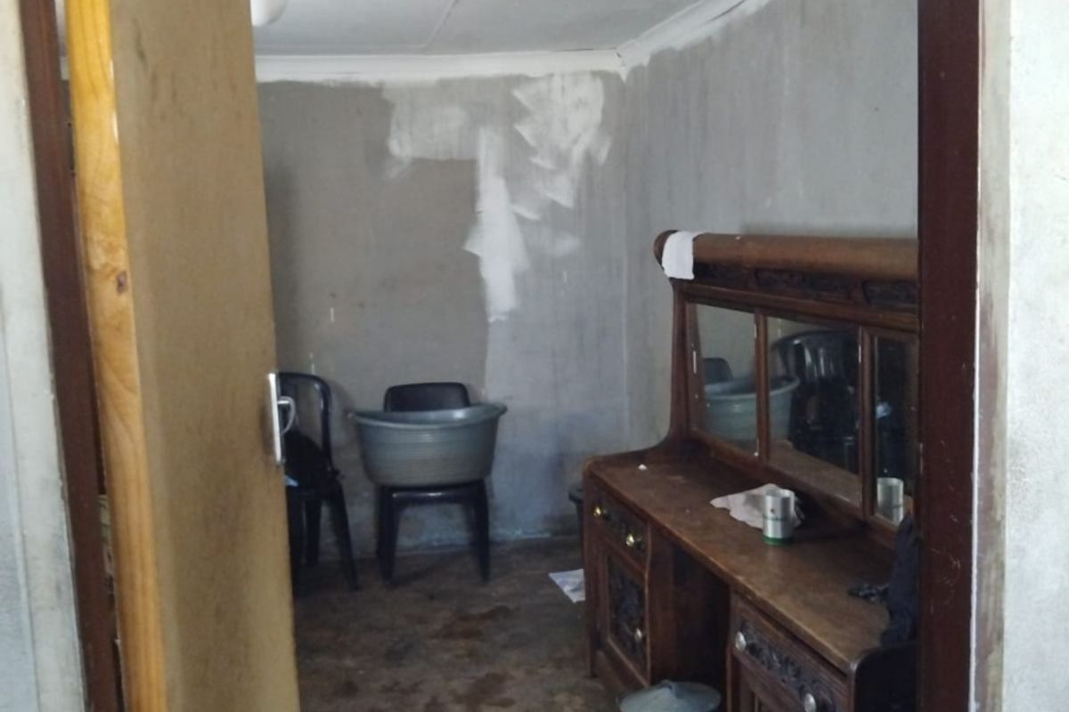 A bedroom space requiring significant renovation, featuring unfinished plaster walls, worn flooring, and dated ceiling finishes.